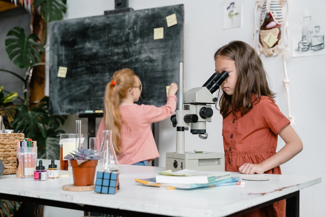 Two girls engaged in a science experiment using a microscope in a classroom setting.